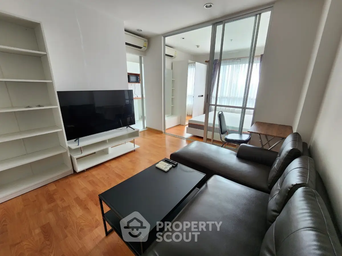 Modern living room with sleek black sofa and large TV, featuring wooden flooring and ample natural light.