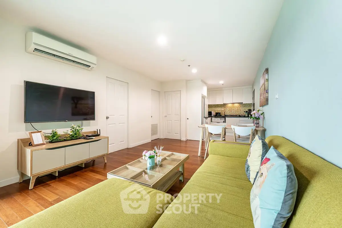 Spacious living room with modern decor and open kitchen layout, featuring a large TV and stylish furniture.