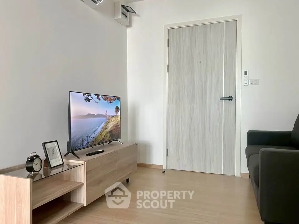 Modern living room with sleek wooden flooring and minimalist decor, featuring a flat-screen TV and cozy seating.