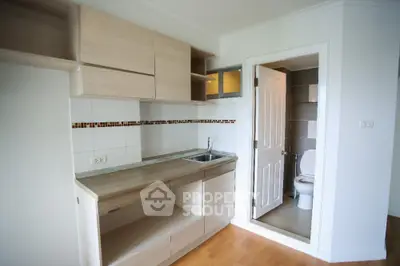 Compact kitchen with light wood cabinetry and adjacent bathroom in modern apartment