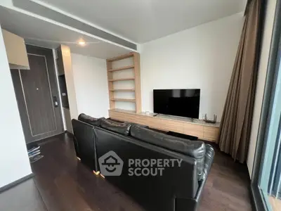 Modern living room with sleek black leather sofa and large TV, featuring wooden shelves and dark flooring.