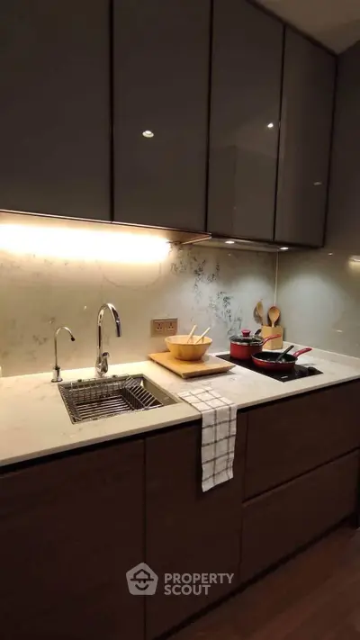 Modern kitchen with sleek cabinetry and under-cabinet lighting, featuring a stylish sink and countertop accessories.