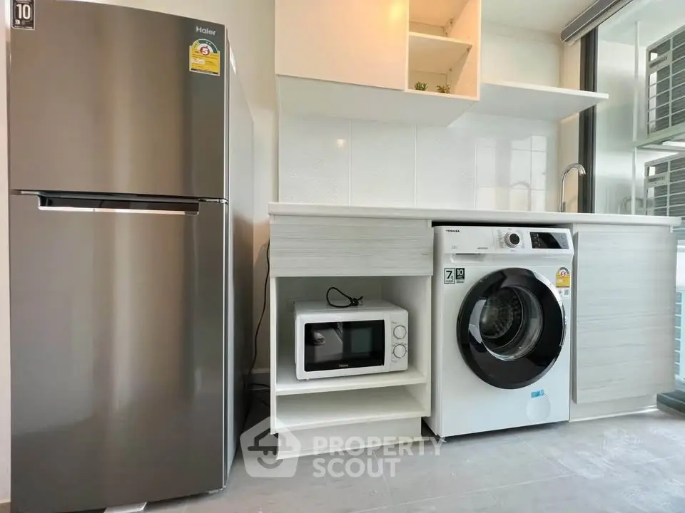 Modern kitchen with stainless steel fridge, washing machine, and microwave in sleek cabinetry.