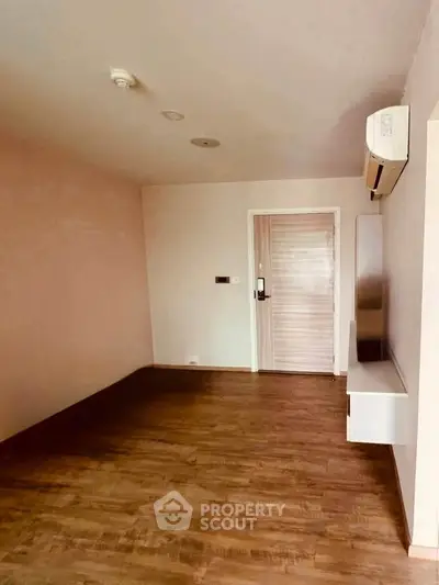 Spacious empty room with wooden flooring and air conditioning, perfect for customization.