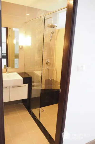 Modern bathroom with glass shower enclosure, sleek fixtures, and warm beige tiles, reflecting a blend of comfort and style.