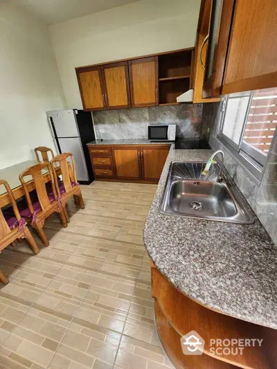 Spacious kitchen with granite countertops, wooden cabinets, and dining area, featuring a fridge and microwave.