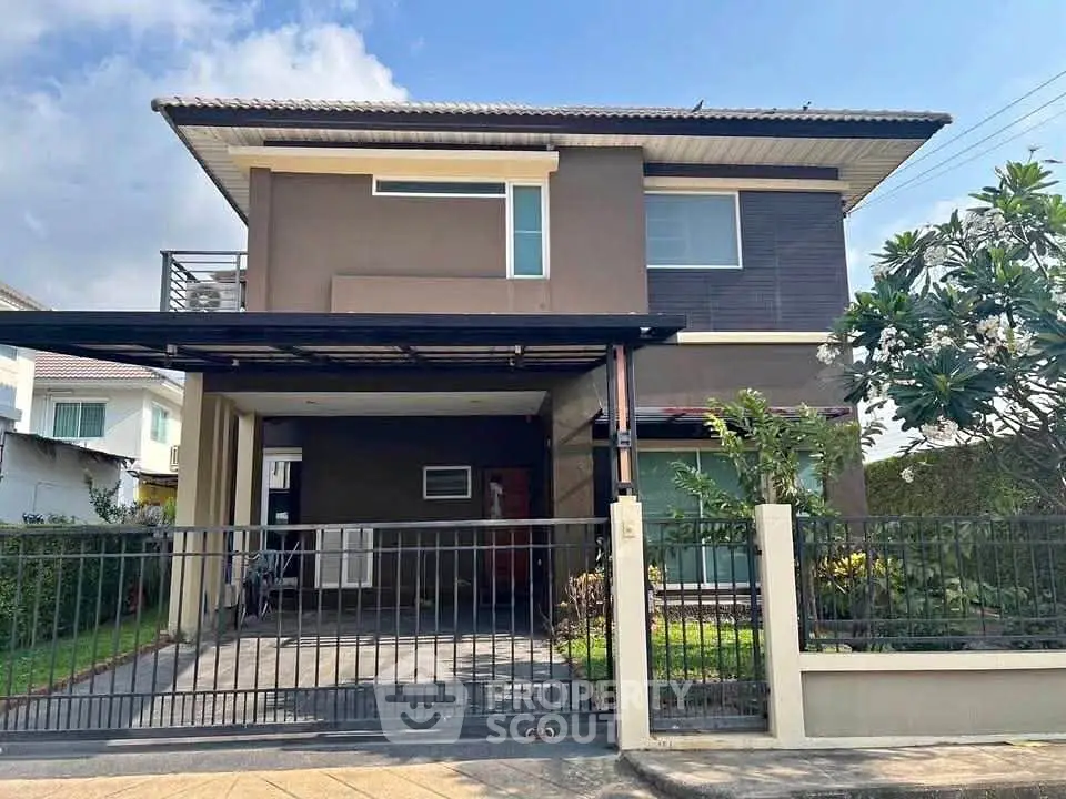 Modern two-story house with gated driveway and lush garden in a serene neighborhood.