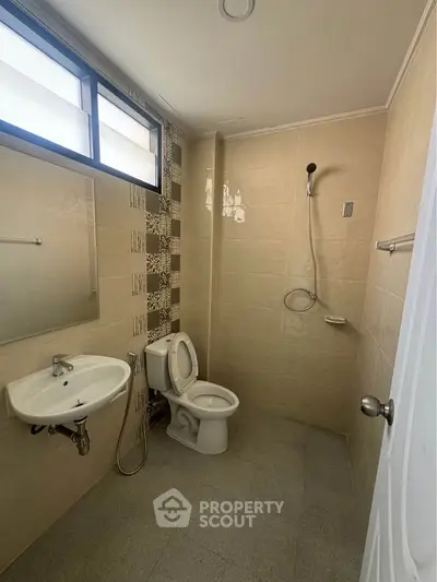 Modern bathroom with beige tiles, wall-mounted sink, and shower area.