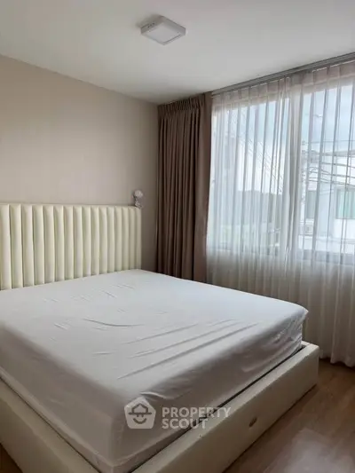 Modern bedroom with large window and elegant bed frame, offering natural light and cozy ambiance.