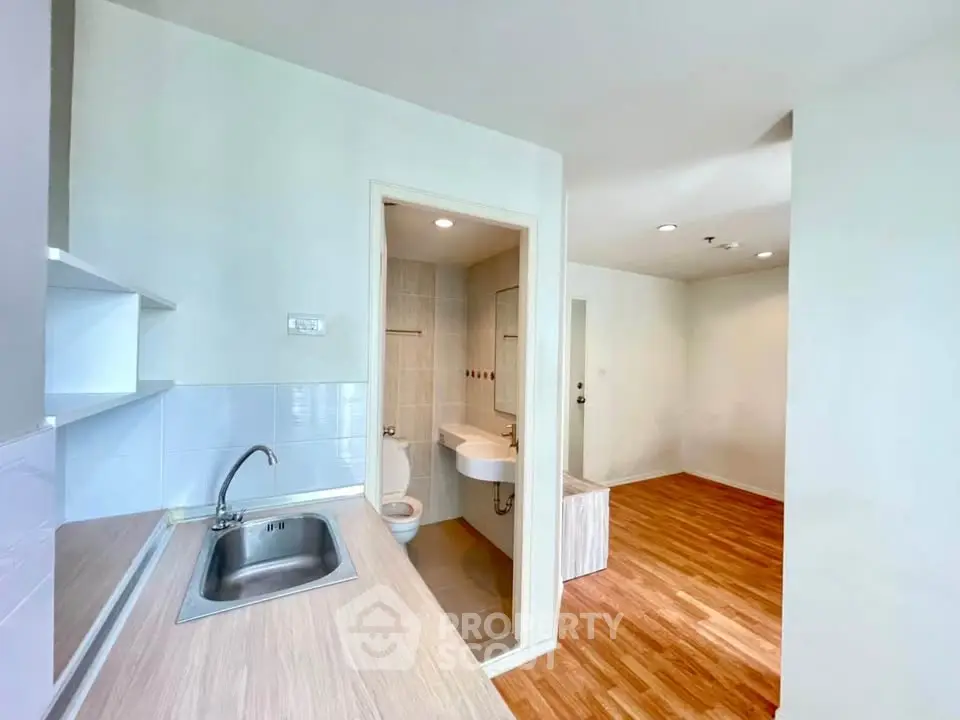 Modern apartment interior with compact kitchen and bathroom, featuring sleek fixtures and wooden flooring.