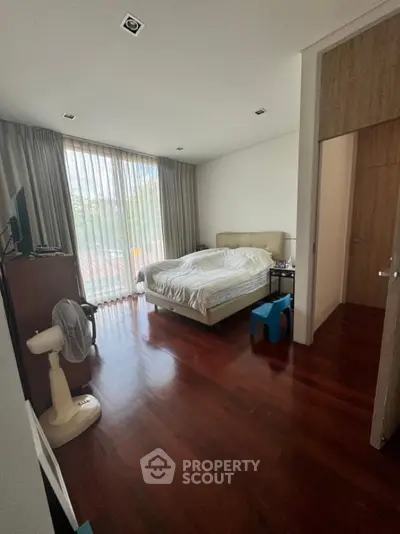 Spacious bedroom with wooden flooring and large window for natural light