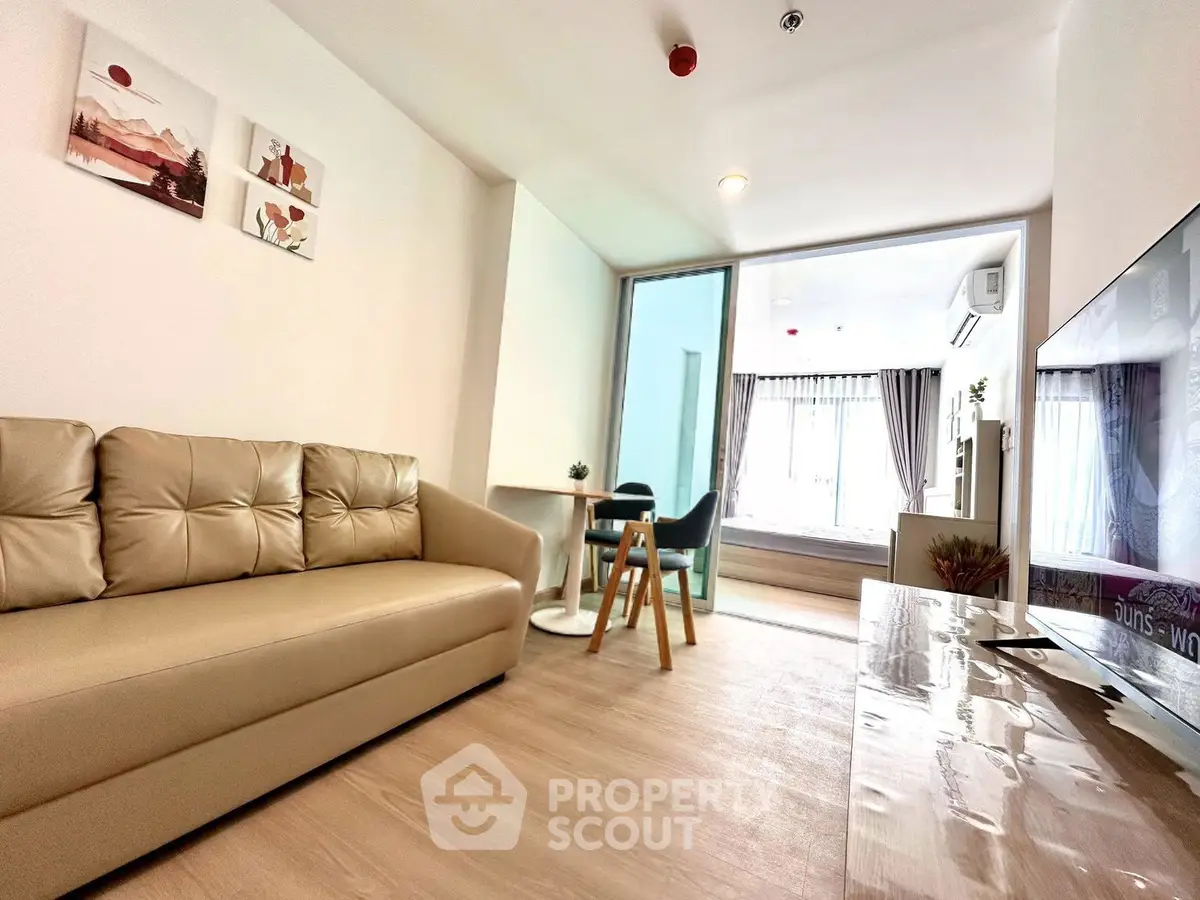 Modern living room with beige sofa and open layout leading to a bright dining area.