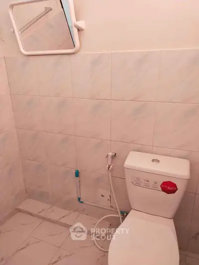 Simple bathroom with white tiles and toilet, featuring a wall-mounted mirror.