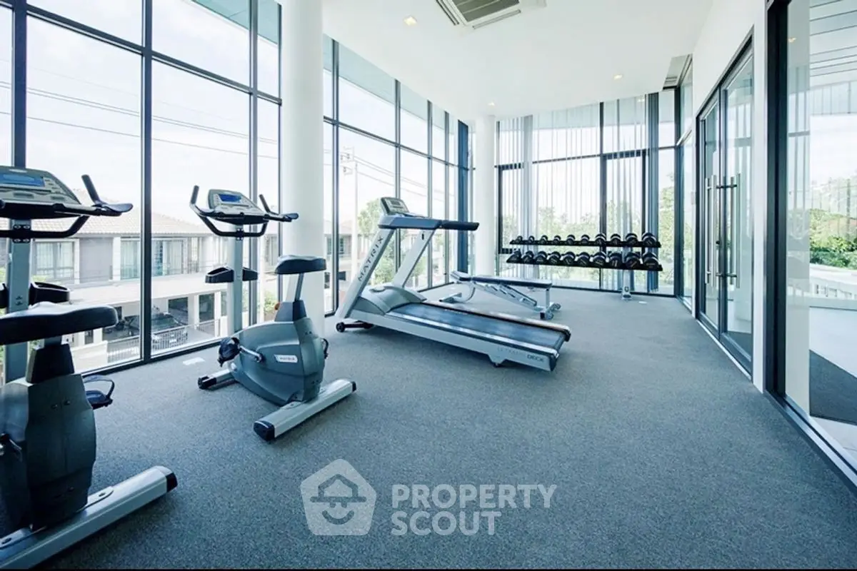 Modern gym with large windows and fitness equipment in luxury apartment complex.