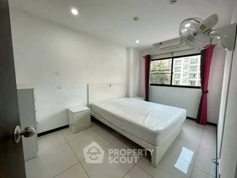 Spacious bedroom with natural light and modern furnishings in urban apartment.