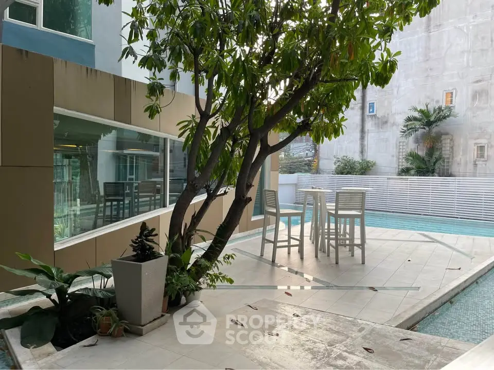 Modern outdoor pool area with stylish seating and lush greenery in a contemporary building setting.