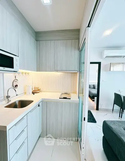 Modern kitchen with sleek cabinetry and built-in microwave, adjacent to a cozy living area.