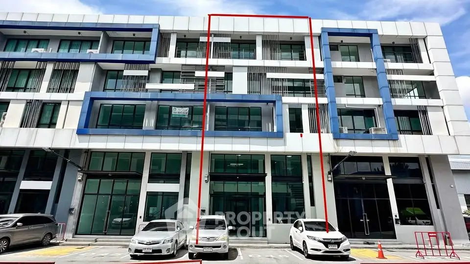Modern commercial building with large glass windows and parking area in front.