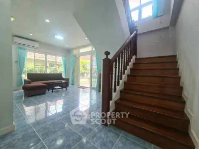 Spacious living room with elegant staircase and large windows offering natural light.