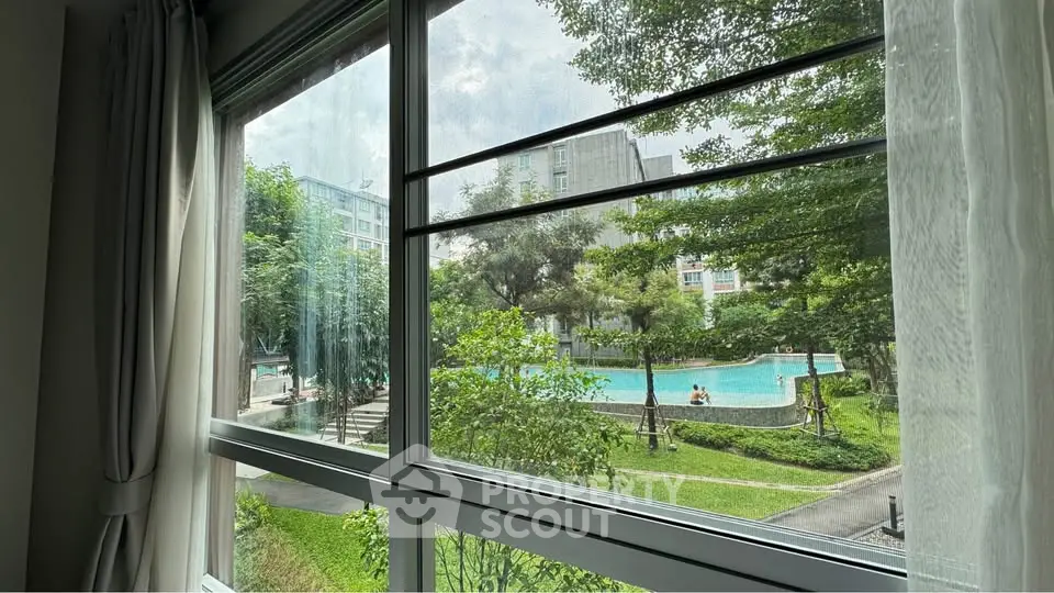 Stunning view of lush garden and pool from a cozy apartment window, perfect for relaxation and leisure.