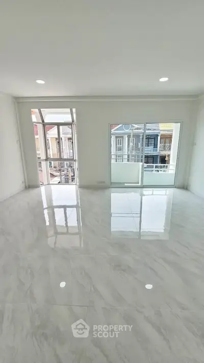 Spacious living room with large windows and balcony access, featuring glossy marble flooring and abundant natural light.