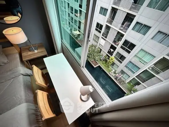 Modern bedroom with large window overlooking pool and neighboring building, featuring sleek desk and lamp.