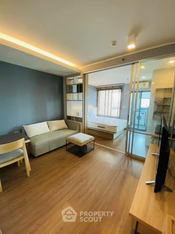 Modern living room with wooden flooring and sliding glass doors leading to a cozy bedroom.