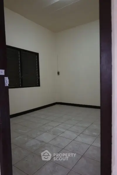 Spacious empty room with tiled flooring and window, ideal for customization.