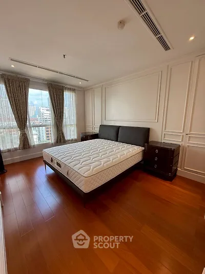 Spacious bedroom with elegant design and city view, featuring hardwood floors and large windows.