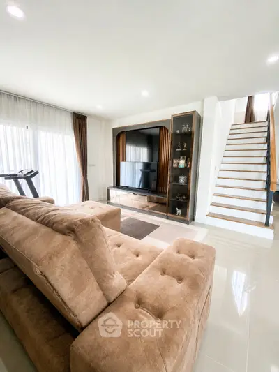 Spacious living room with modern decor and elegant staircase, perfect for family gatherings.