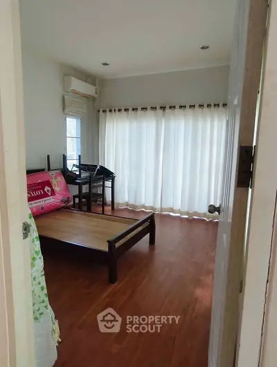 Spacious bedroom with wooden flooring and large windows for natural light.