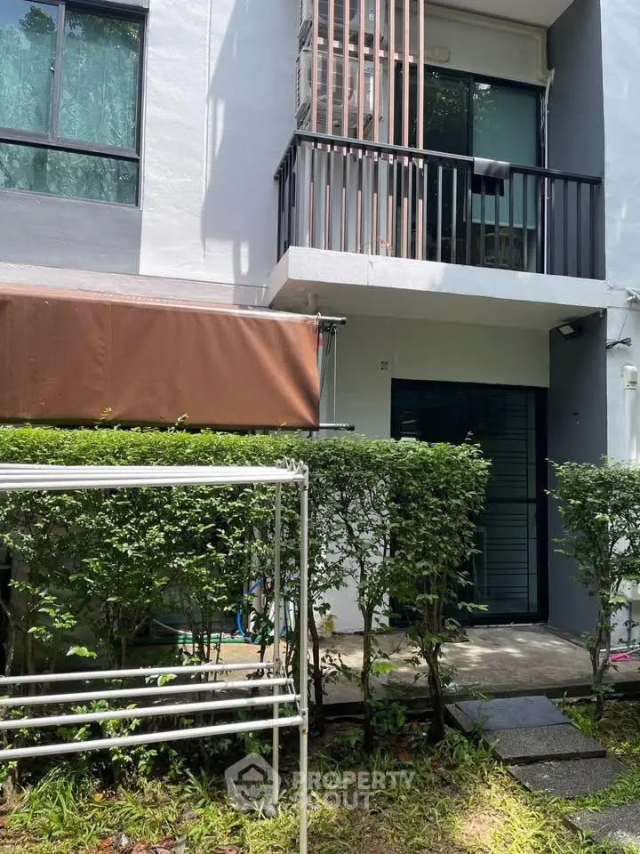 Charming townhouse exterior with lush greenery and private balcony, perfect for serene living.