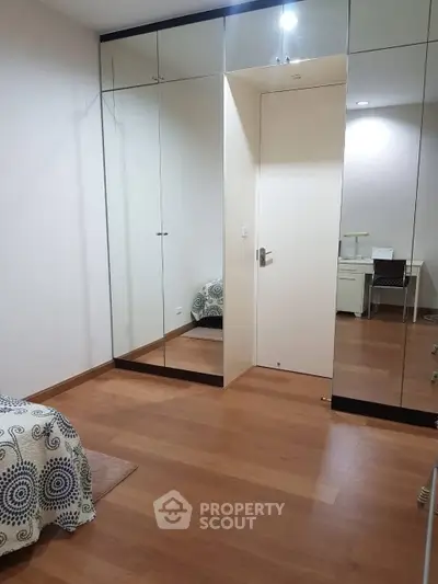 Spacious bedroom with mirrored closet doors and wooden flooring