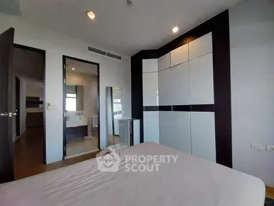 Spacious modern bedroom with sleek built-in wardrobe and ensuite bathroom in luxury apartment.