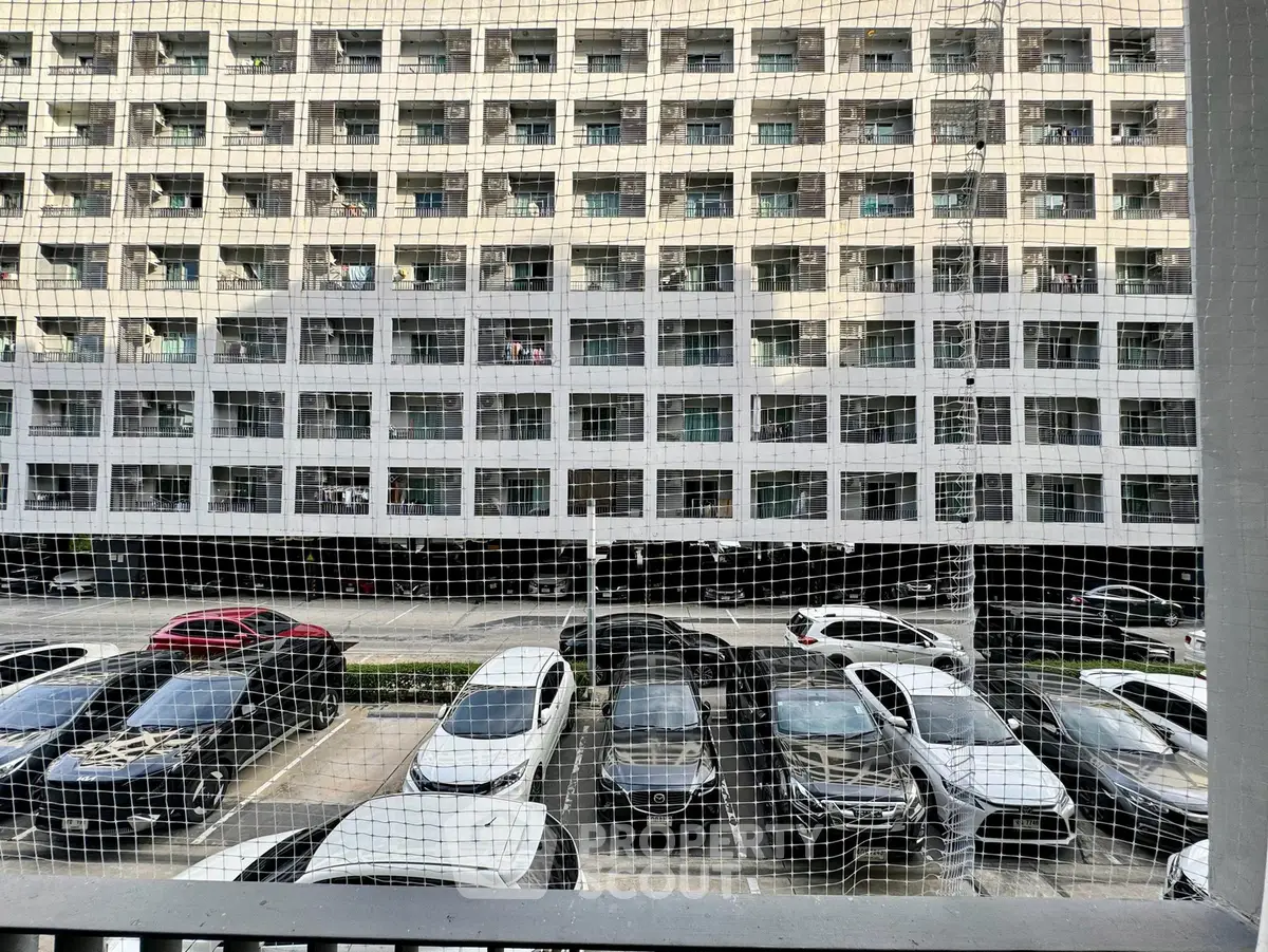 Modern apartment building with spacious parking area and multiple vehicles parked.