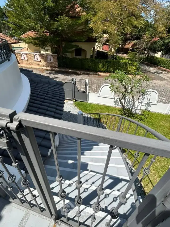 Elegant exterior staircase with wrought iron railing leading to lush garden view.