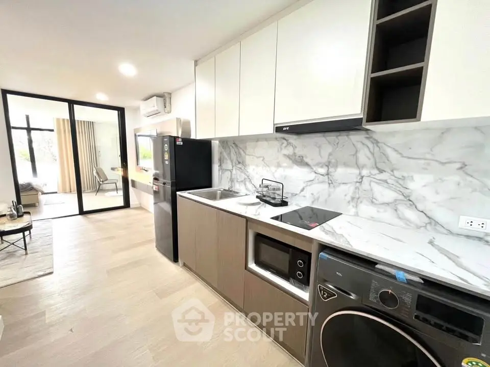 Modern kitchen with marble backsplash, sleek appliances, and open layout leading to a bright living area.