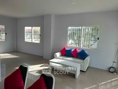 Spacious living room with modern decor and natural light, featuring a cozy white sofa and vibrant cushions.