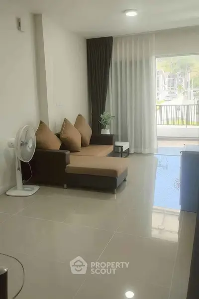 Modern living room with sleek sofa and large window overlooking balcony, offering bright and airy ambiance.