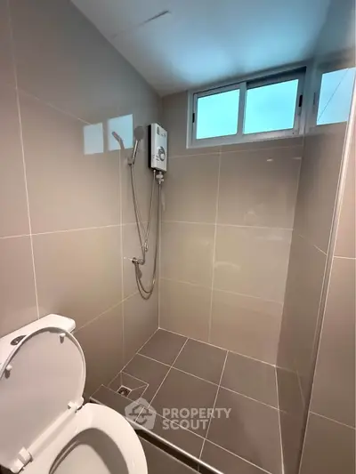 Modern bathroom with sleek tiles and shower unit, featuring a compact design and natural light from a window.
