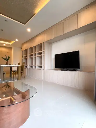 Modern living room with built-in shelves and flat-screen TV, featuring elegant lighting and sleek furniture.