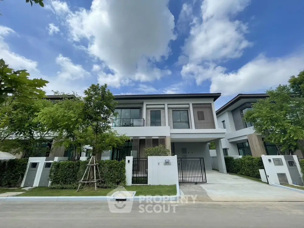 Modern two-story house with lush greenery and spacious driveway under a clear blue sky.