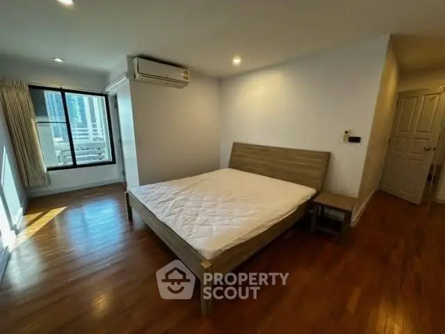 Spacious bedroom with wooden flooring and large window view