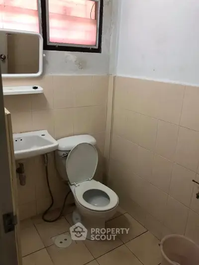 Compact bathroom with toilet, sink, and wall-mounted mirror in a tiled setting.