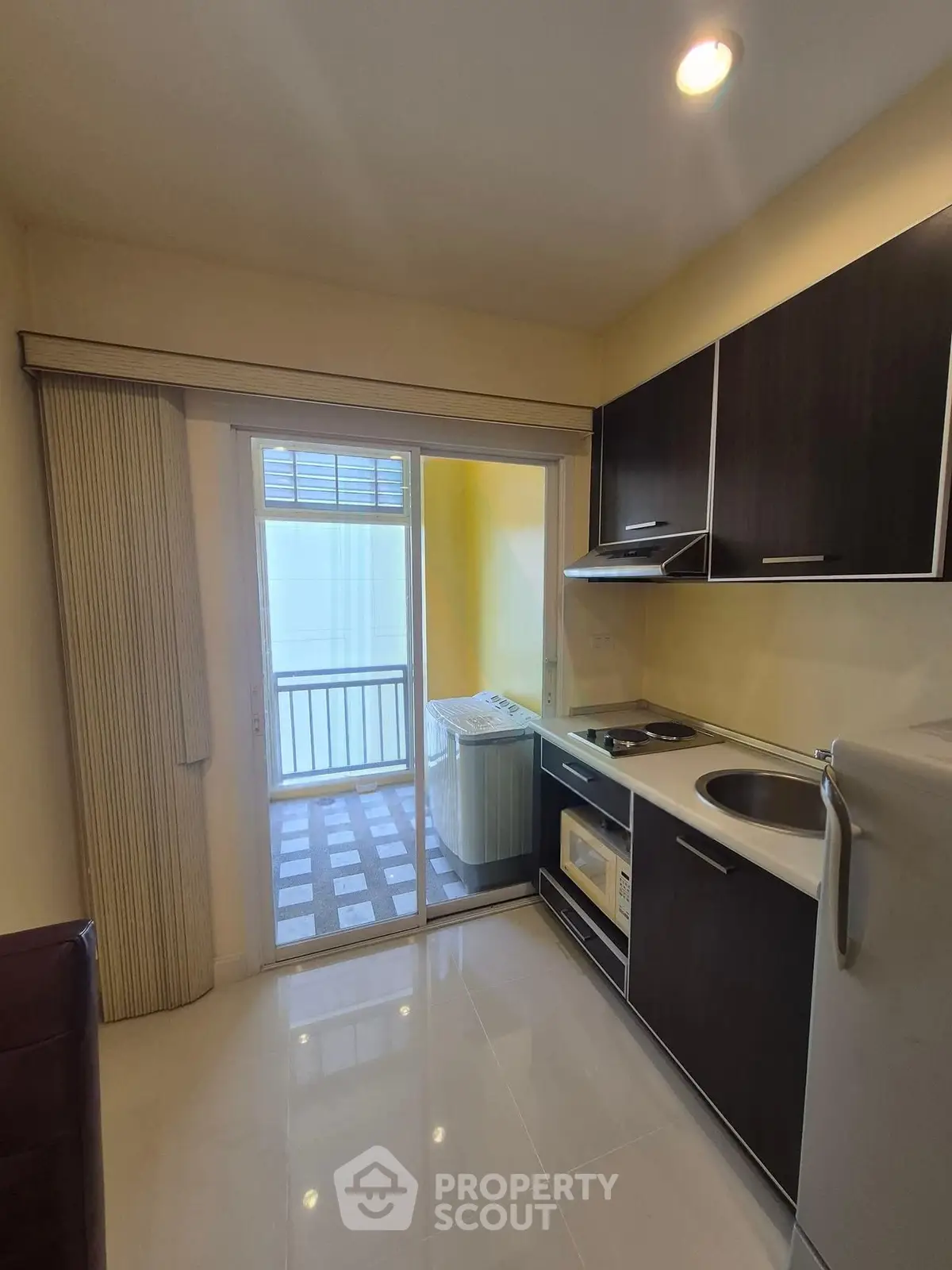 Modern kitchen with sleek cabinetry and balcony access, featuring a washing machine and compact appliances.