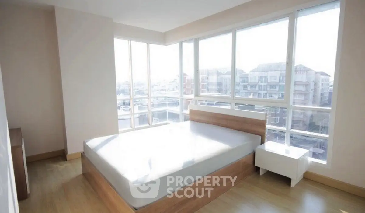 Bright bedroom with large windows and city view, featuring modern wooden bed and nightstand.