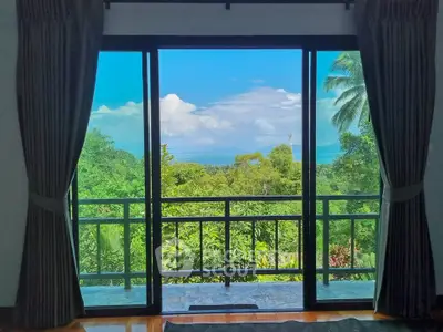 Stunning view from a living room with large glass doors opening to lush greenery and ocean horizon.