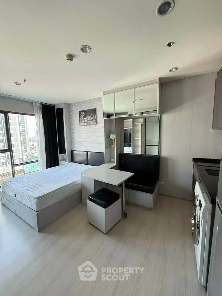 Modern studio apartment with bed, dining area, and washing machine, featuring city view.
