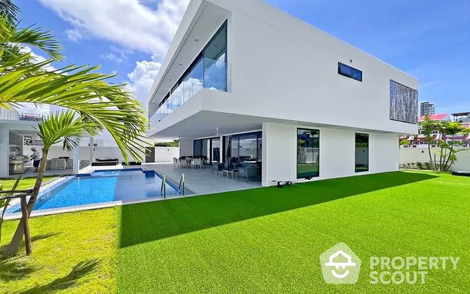 Luxurious modern villa with pool and lush green lawn under clear blue sky