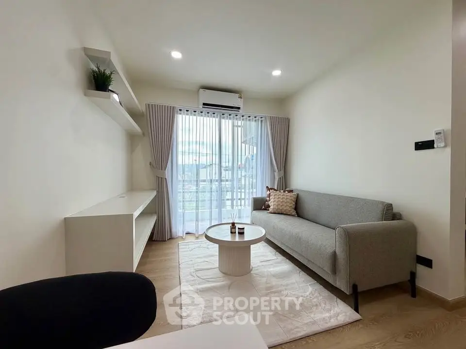 Modern living room with sleek sofa, stylish decor, and natural light from large window.